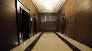 A hallway with a chandelier, elevators, and a reflective floor.