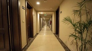 A hotel corridor with doors on both sides, a tiled floor, and a plant on the right. - Duplex w/ Pool View Near AUC (New Cairo City)