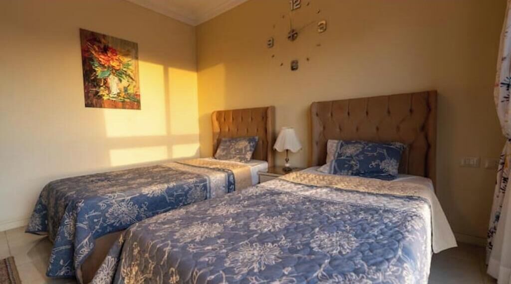 Een hotelkamer met twee bedden, elk met hoofdbord en passend kussen. Er hangt een wandklok en een schilderij aan de muur.