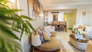 A living room with a sofa, a coffee table, and a dining area with chairs and a table. - Duplex w/ Pool View Near AUC (New Cairo City)