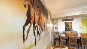 A dining area with a mural of horses on the wall, wooden furniture, and a visible kitchen area in the background. - Duplex w/ Pool View Near AUC (New Cairo City)