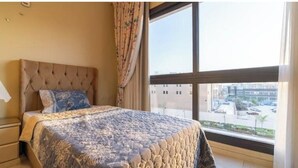 A bedroom with a large bed, a window with a view of buildings, and a curtain. - Duplex w/ Pool View Near AUC (New Cairo City)