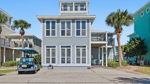 A two-story building with a balcony, a golf cart in the driveway, and palm trees.