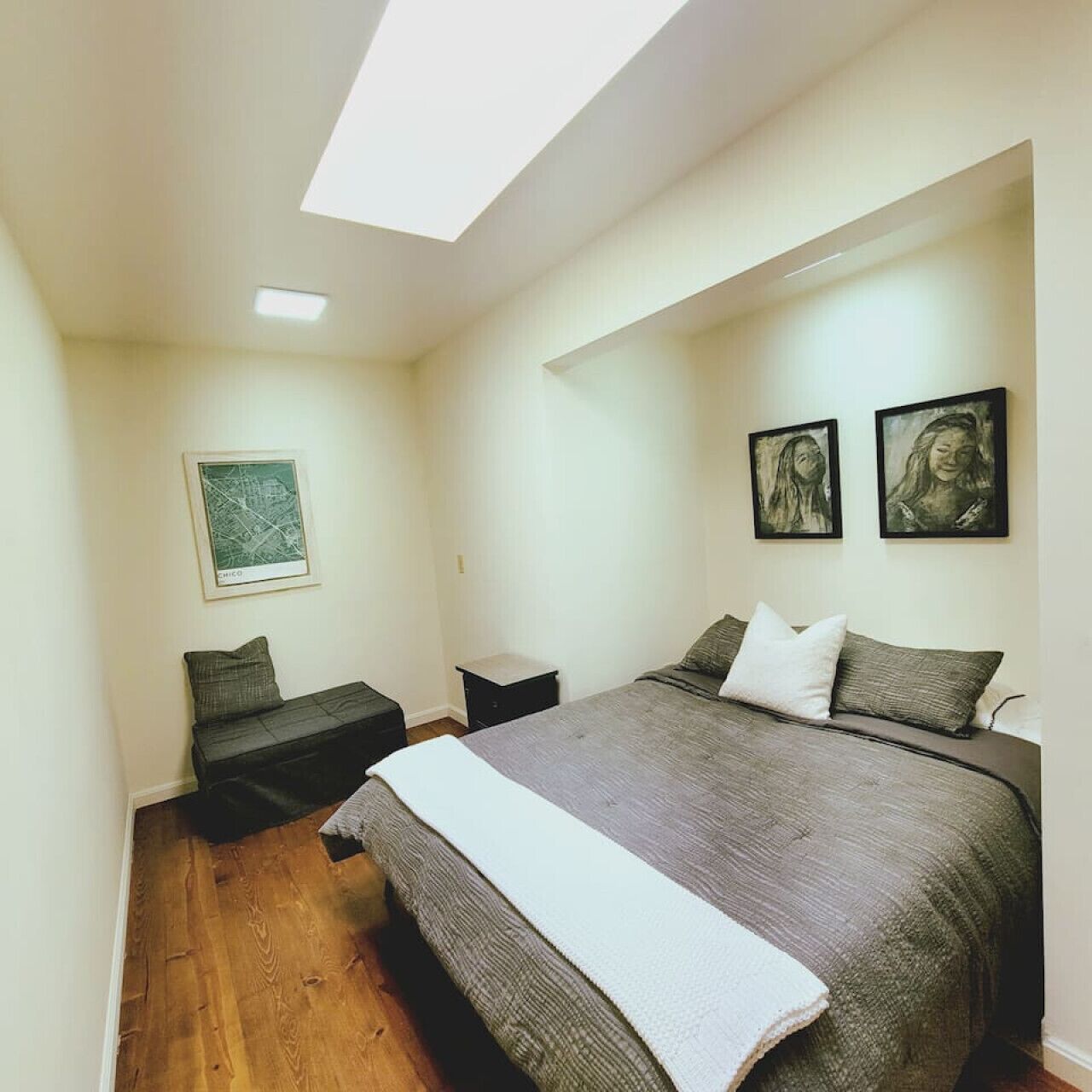 A bedroom with a bed, a nightstand, a small table, and a map on the wall.