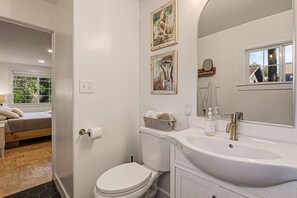 Une salle de bain moderne avec des toilettes, un lavabo et un miroir. Deux œuvres d’art encadrées ornent le mur.