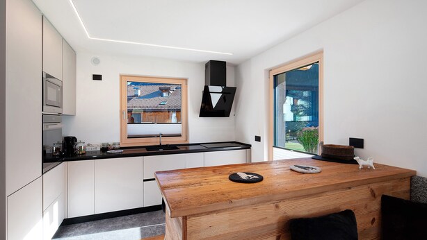 A modern kitchen with white cabinets, a wooden dining table, and a window with a view of greenery. - Apartment 'Cesa Pattis' with Mountain View, Private Garden and Wi-Fi (Mazzin)