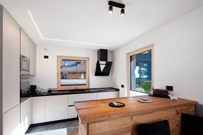 Una cocina moderna con armarios blancos, una mesa de comedor de madera y un ventanal con vistas a la vegetación.