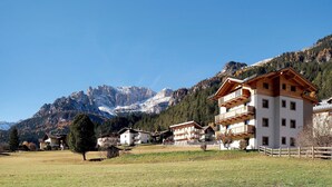A mountain resort with chalet-style buildings, a clear sky, and snow-capped peaks in the background. - Apartment 'Cesa Pattis' with Mountain View, Private Garden and Wi-Fi (Mazzin)