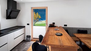 A modern kitchen with a black range hood, a wooden dining table, and a view of a garden through a sliding door. - Apartment 'Cesa Pattis' with Mountain View, Private Garden and Wi-Fi (Mazzin)