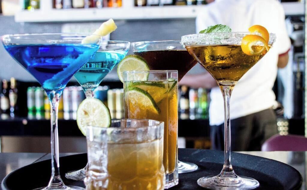 Diverse cocktails op een barachtergrond, met een vage achtergrond van flessen op planken.