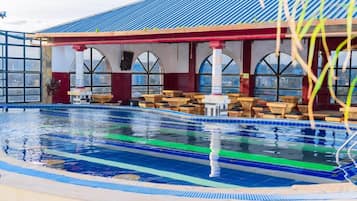 Piscina com espreguiçadeiras e área de estar coberta com janelas em arco.