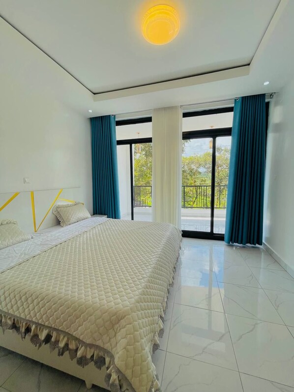A bedroom with a large bed, a balcony, and a view of greenery.