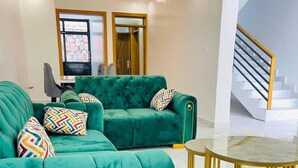 Een moderne woonkamer met smaragdgroene banken, een gele fauteuil en een salontafel met glazen blad.