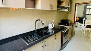 Een moderne keuken met beige kastjes, een zwart aanrecht, een ingebouwde oven en een koffiezetapparaat.