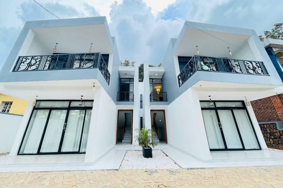 A modern two-story house with a symmetrical design, featuring large windows, balconies, and a central staircase.