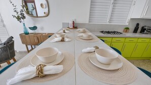 A dining table set with white plates, bowls, and napkins, surrounded by green cabinets and a kitchen area. - Sunset Marena/Beach Front House (Stella)