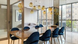 Un comedor moderno con mesa de vidrio y sillas azules, ventanas amplias y lámparas esféricas colgantes.