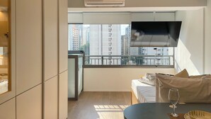 Habitación de hotel moderna con balcón, televisión de pantalla plana, cama, mesa de comedor y vistas a la ciudad.