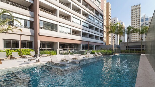 Una piscina con sillas de descanso y un edificio moderno con balcones al fondo.
