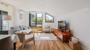 Un salon moderne comprenant un canapé, une table à manger, un téléviseur et un escalier menant à un balcon.