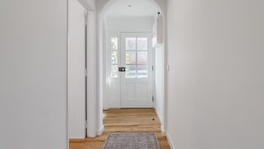 Un couloir aux murs blancs, doté d’un plancher en bois et d’une porte dont les panneaux sont en verre dépoli.