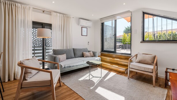Un salon moderne avec un canapé, des fauteuils, une petite table et une vue sur l’extérieur.
