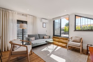 Sala de estar moderna com sofá, cadeiras, uma mesa pequena e vista para o exterior.