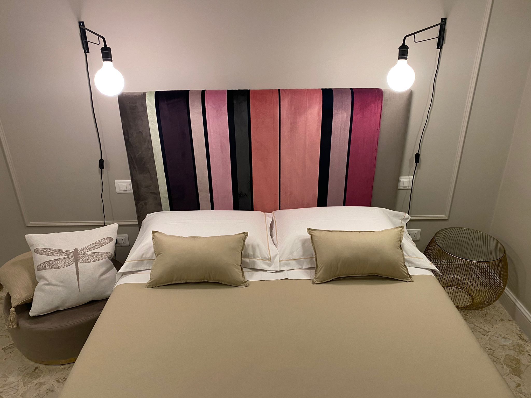 Un dormitorio con una cama, dos lámparas de noche, un cabecero con rayas verticales y una mesita de noche con lámpara.