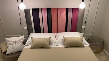 Un dormitorio con una cama, dos lámparas de noche, un cabecero con rayas verticales y una mesita de noche con lámpara.