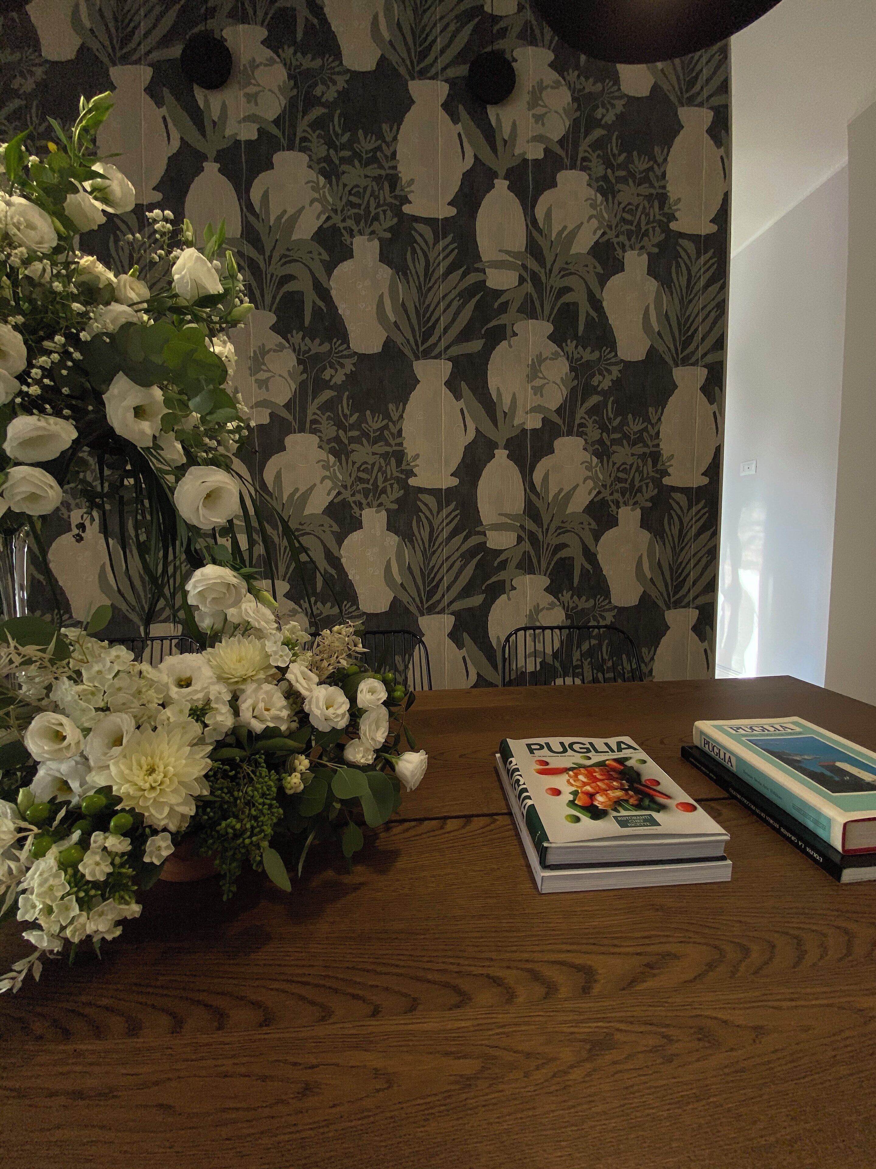 A wooden table with a floral arrangement and two books titled 'Puglia'.