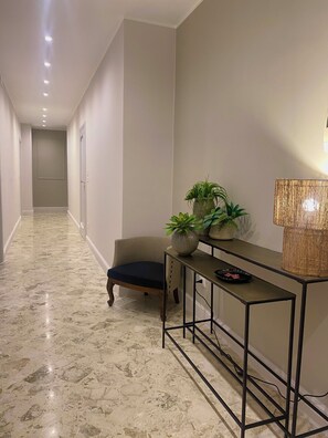 A hallway with a marble floor, a chair, a console table with plants, and a lamp. - Casa Almika Sparano (Bari)