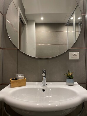 A bathroom with a white sink, a round mirror, and a small potted plant. - Casa Almika Sparano (Bari)