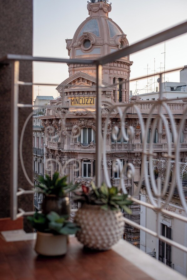 A balcony with a wrought iron railing, a potted plant, and a view of a historic building labeled "MINCUZZI". - Casa Almika Sparano (Bari)