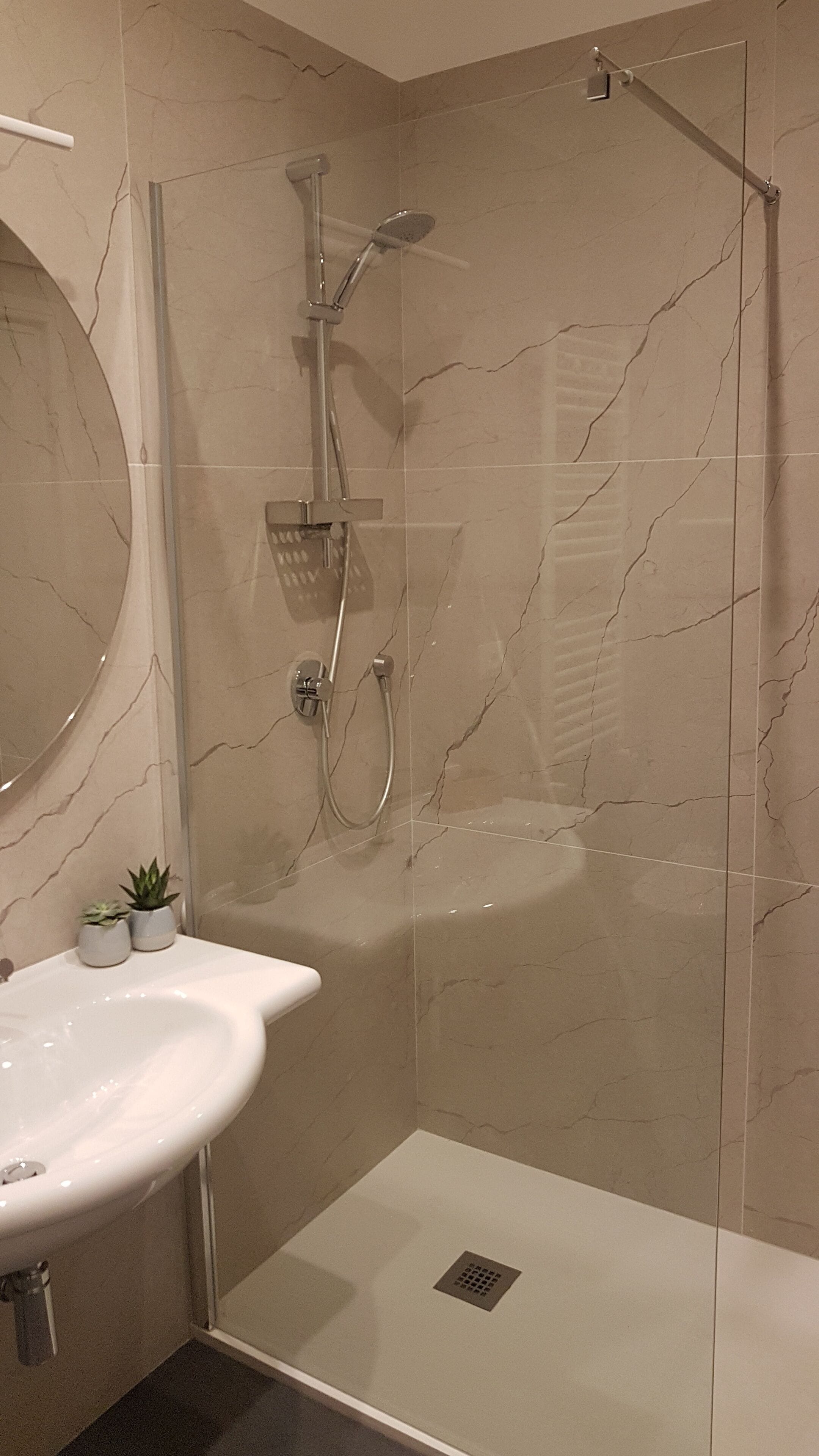 Un baño moderno con ducha de mampara de vidrio, un lavamanos blanco y una pared revestida de mármol.
