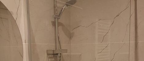 Un baño moderno con ducha de mampara de vidrio, un lavamanos blanco y una pared revestida de mármol.