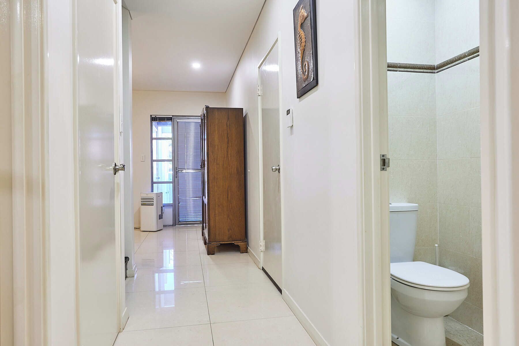 A hallway leading to a bathroom with a toilet and a shower area.
