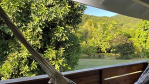 Eine Hängematte auf einer Holzterrasse mit Blick auf eine üppige, grüne Landschaft und Hügel im Hintergrund.