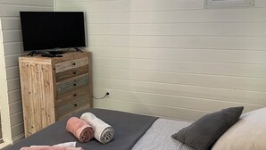 Ein Schlafzimmer mit einem Bett, einem Fernseher auf einer Holzkommode und einem Fenster.