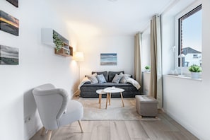 A modern living room with a grey sofa, a round coffee table, a grey armchair, and a window with curtains. - Accessible Apartment 'Landräume' with Wi-Fi (Lunden)