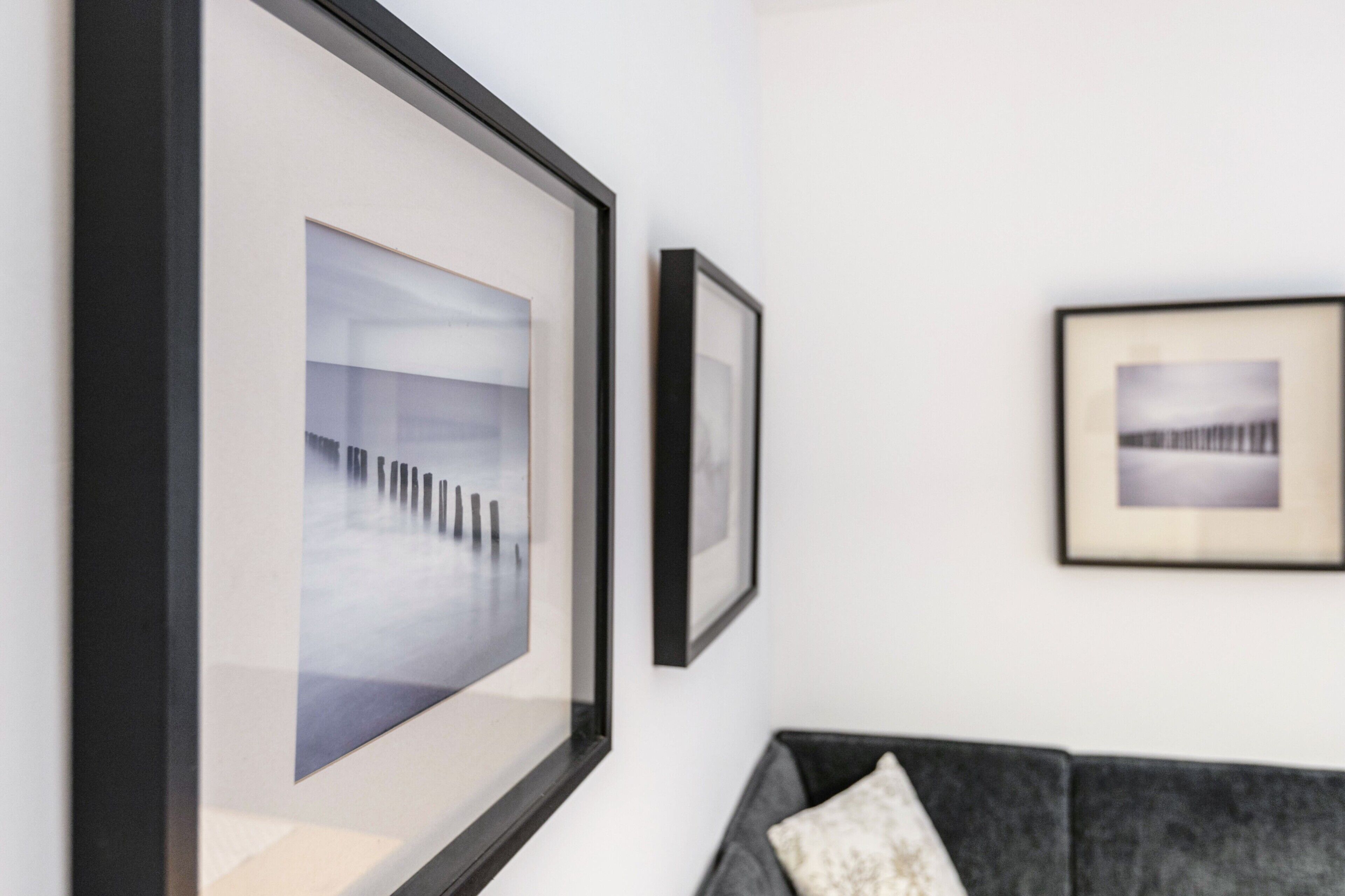 Una habitación con un sofá gris, un cuadro enmarcado en la pared y una pared blanca.