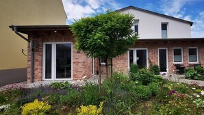 Una casa de dos pisos con fachada de ladrillo, un ventanal grande y un jardín con diversas plantas y flores.