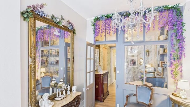 A room with a large ornate mirror, a chandelier, and a door adorned with purple flowers. - Jol Tourisme (Troyes)