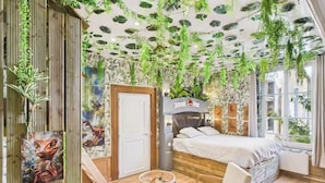 A bedroom with a bed, a chair, a small table, and a wall with hanging plants. - Jol Tourisme (Troyes)