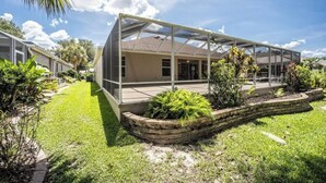 Una casa con un patio cubierto, césped y un jardín con diversas plantas.