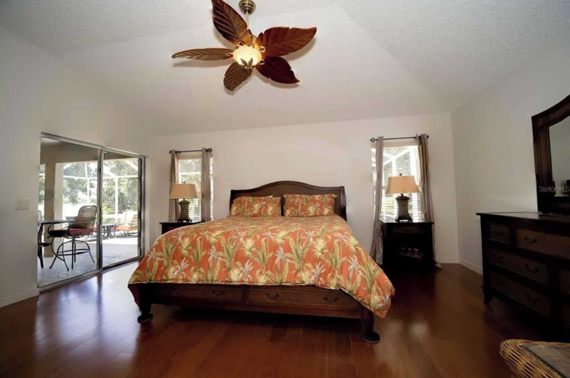 A bedroom with a wooden bed, a ceiling fan, and a view of the outdoors through a sliding glass door.