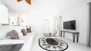 Una sala de estar moderna con un sofá blanco, una mesa de centro de vidrio, un televisor sobre un mueble bajo y una alfombra estampada.