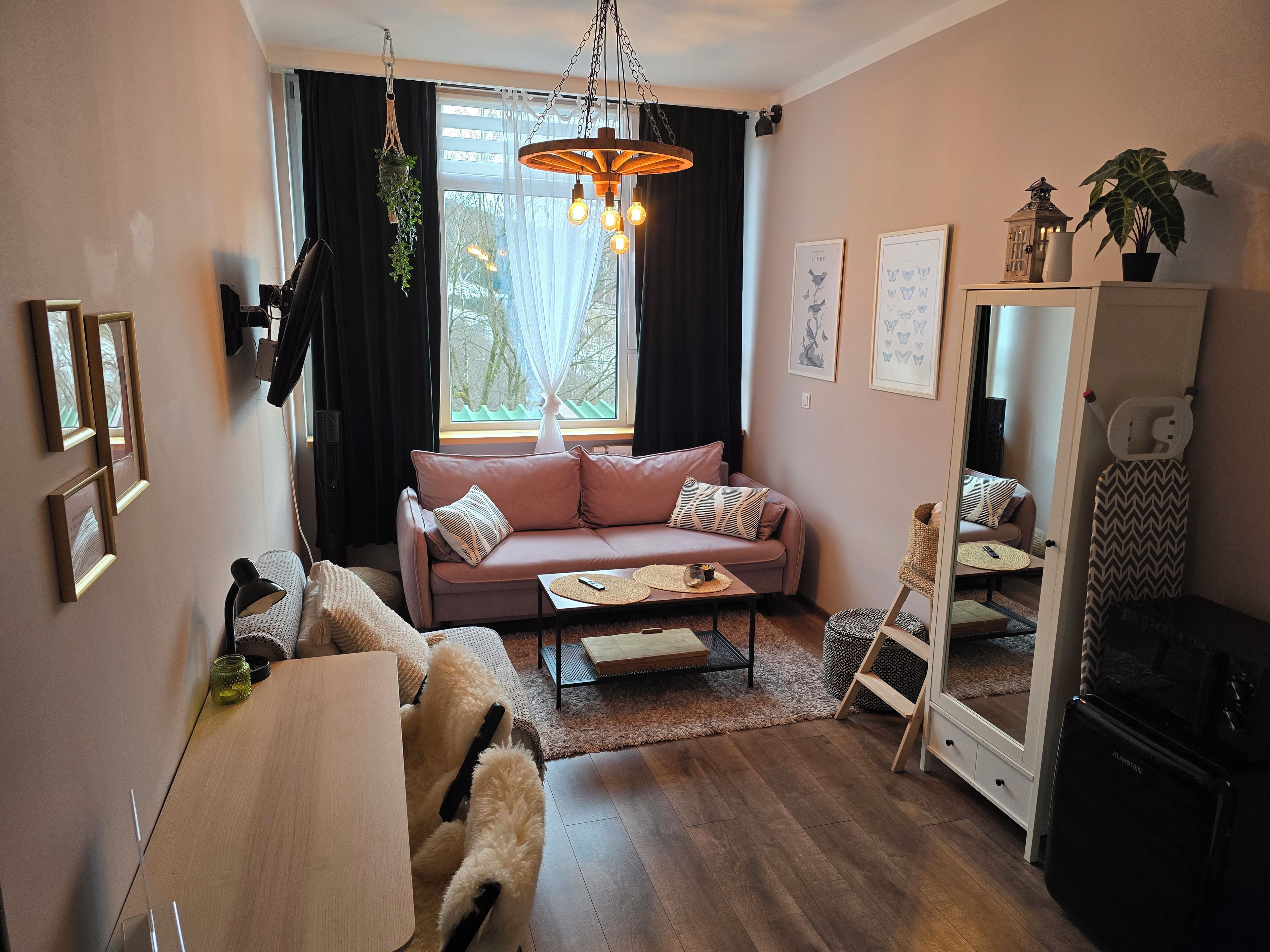 Ett mysigt vardagsrum med en soffa, ett soffbord, en hängande lampa och ett fönster med gardiner.