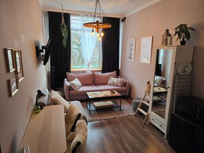 Ett mysigt vardagsrum med en soffa, ett soffbord, en hängande lampa och ett fönster med gardiner.