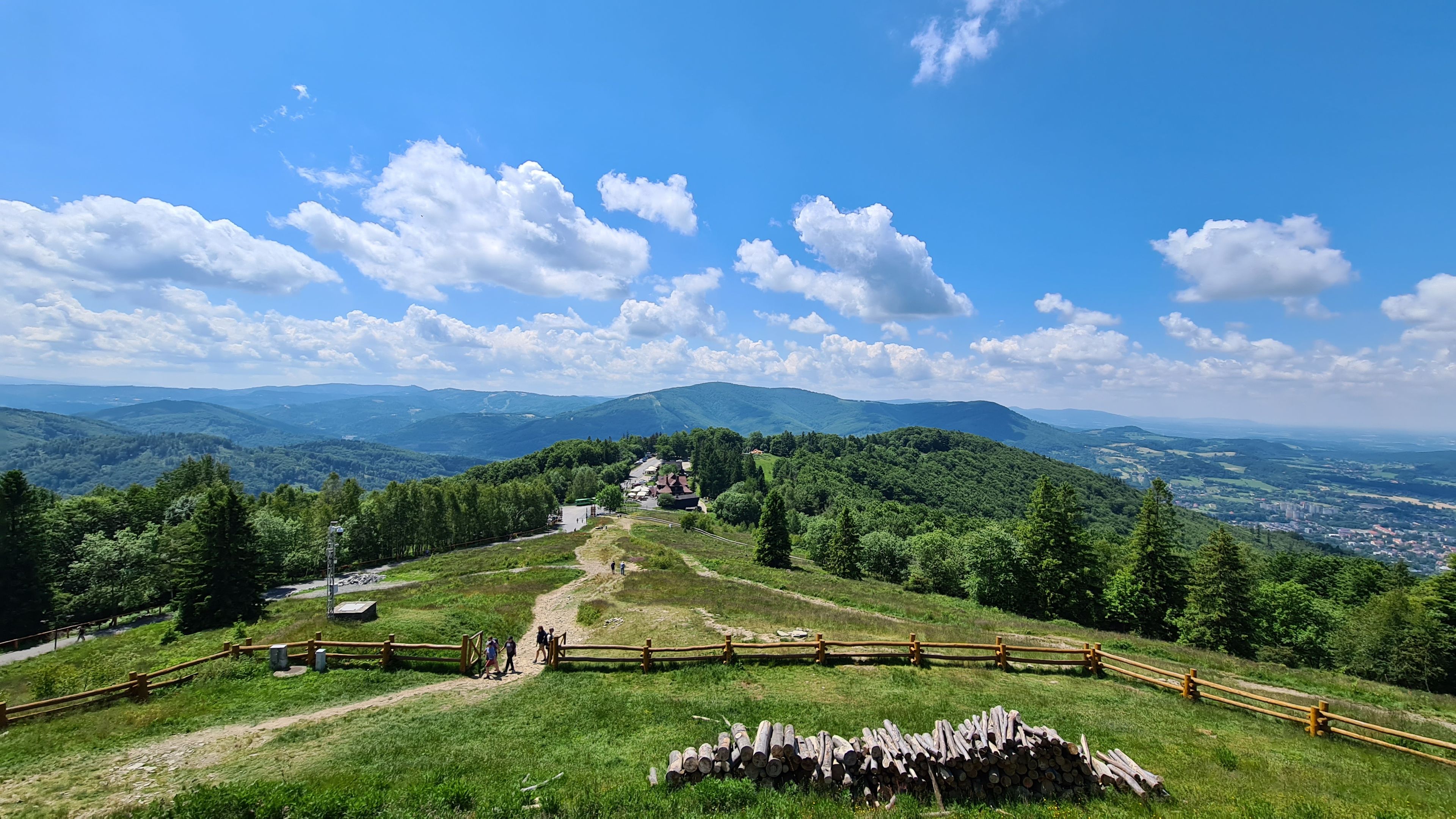 A mountainous landscape with a clear sky, a wooden fence, and a pile of logs.
