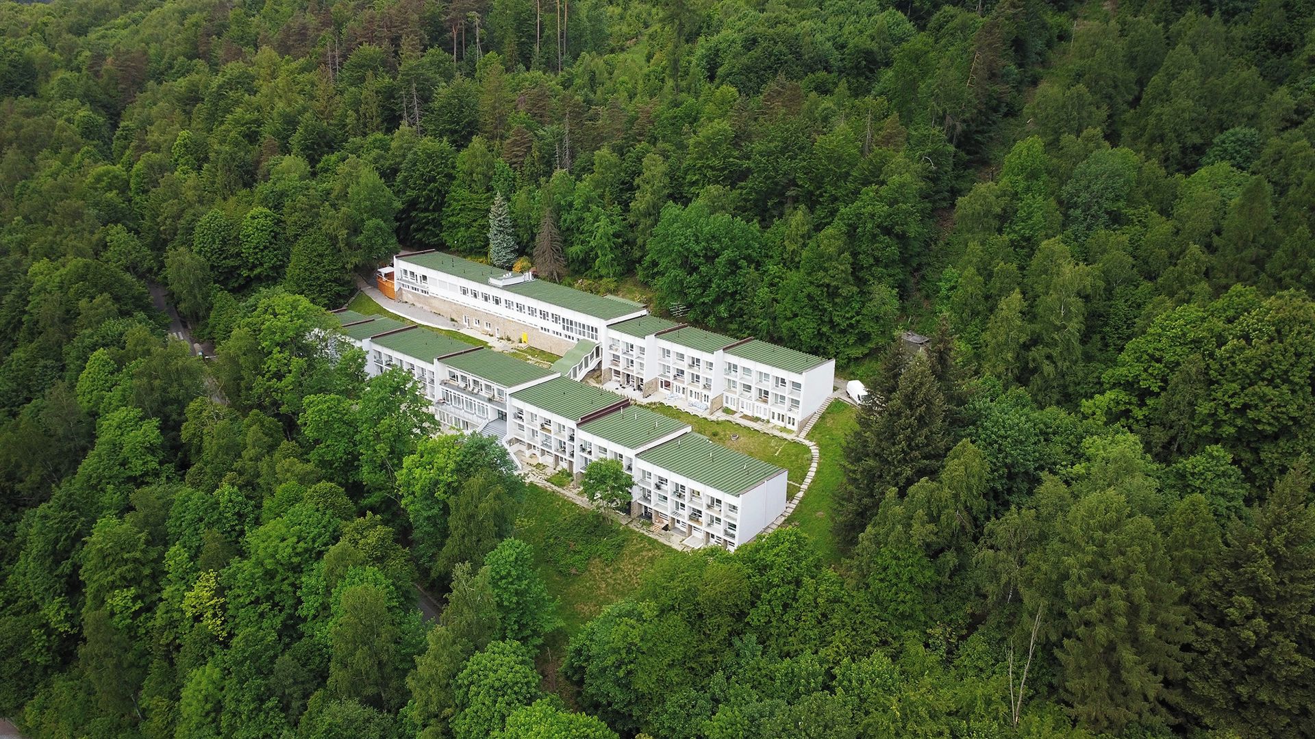 En modern, flervåningsbyggnad med ett platt tak, omgiven av tät skog.